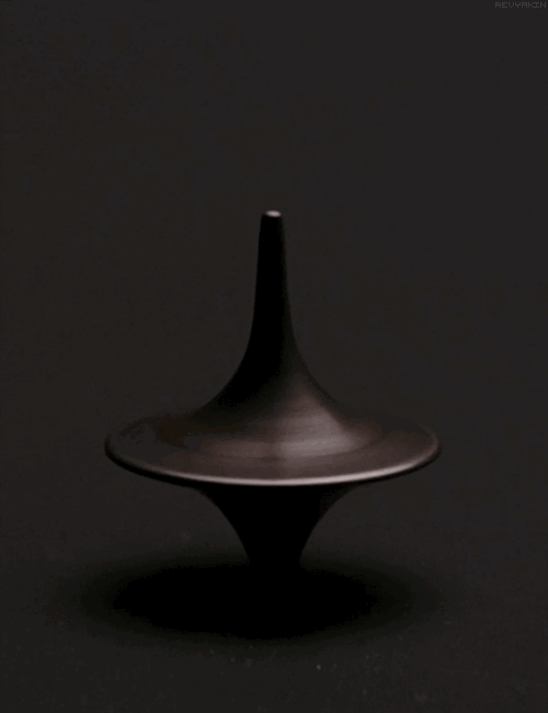 A spinning top made of dark material, rotating smoothly against a black background.
